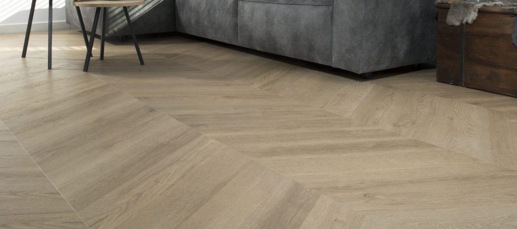 Lichte visgraat PVC vloer in een woonkamer met een grijze hoekbank
