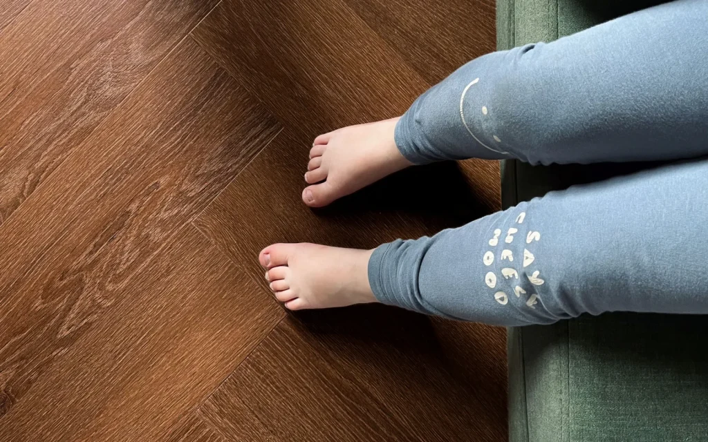 Blote voeten op een donkere houtlook PVC-vloer naast een groene bank