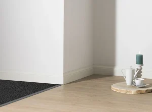 Witte plint langs een lichte houten vloer, met een donkere mat die tegen de plint aanloopt