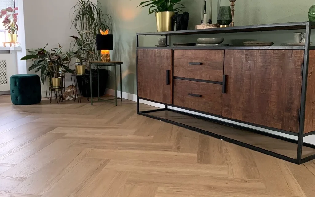 Visgraatvloer van dichtbij met een houten dressoir en planten ertegen