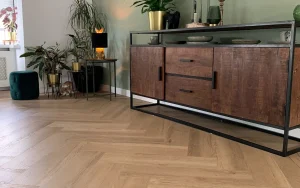 Visgraatvloer van dichtbij met een houten dressoir en planten ertegen