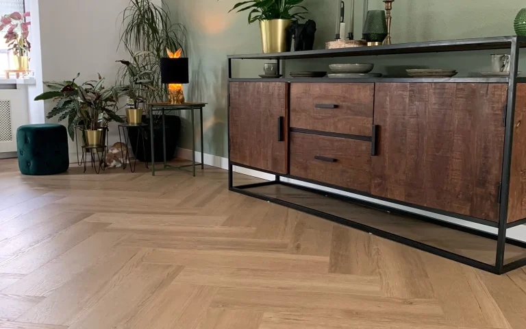 Visgraatvloer van dichtbij met een houten dressoir en planten ertegen
